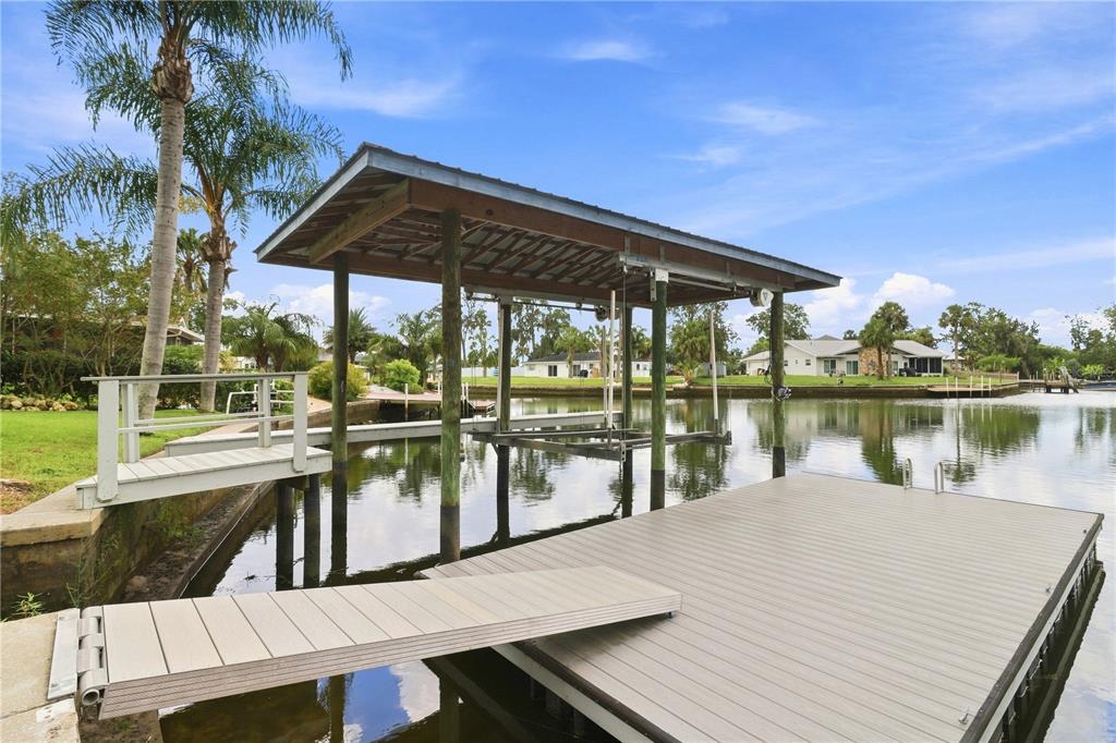 A boat dock with a covered lift extends over a calm canal near residential homes — 1520 SE PINWHEEL DRIVE, CRYSTAL RIVER, FL