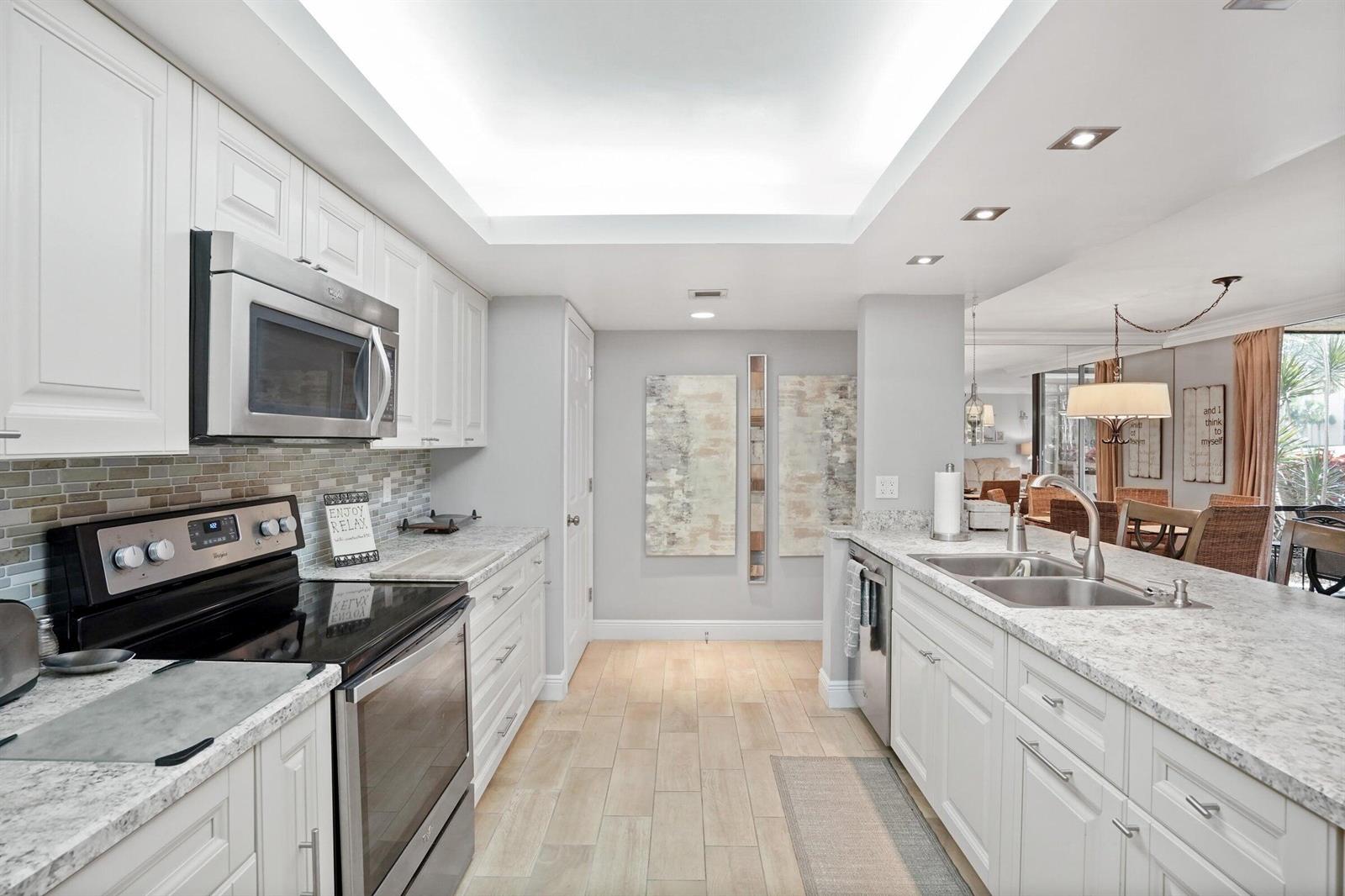 A modern kitchen features white cabinetry, granite countertops, stainless steel appliances, and light wood flooring — 2255 Lindell Boulevard # 4105, Delray Beach FL 33444, DELRAY BEACH, FL