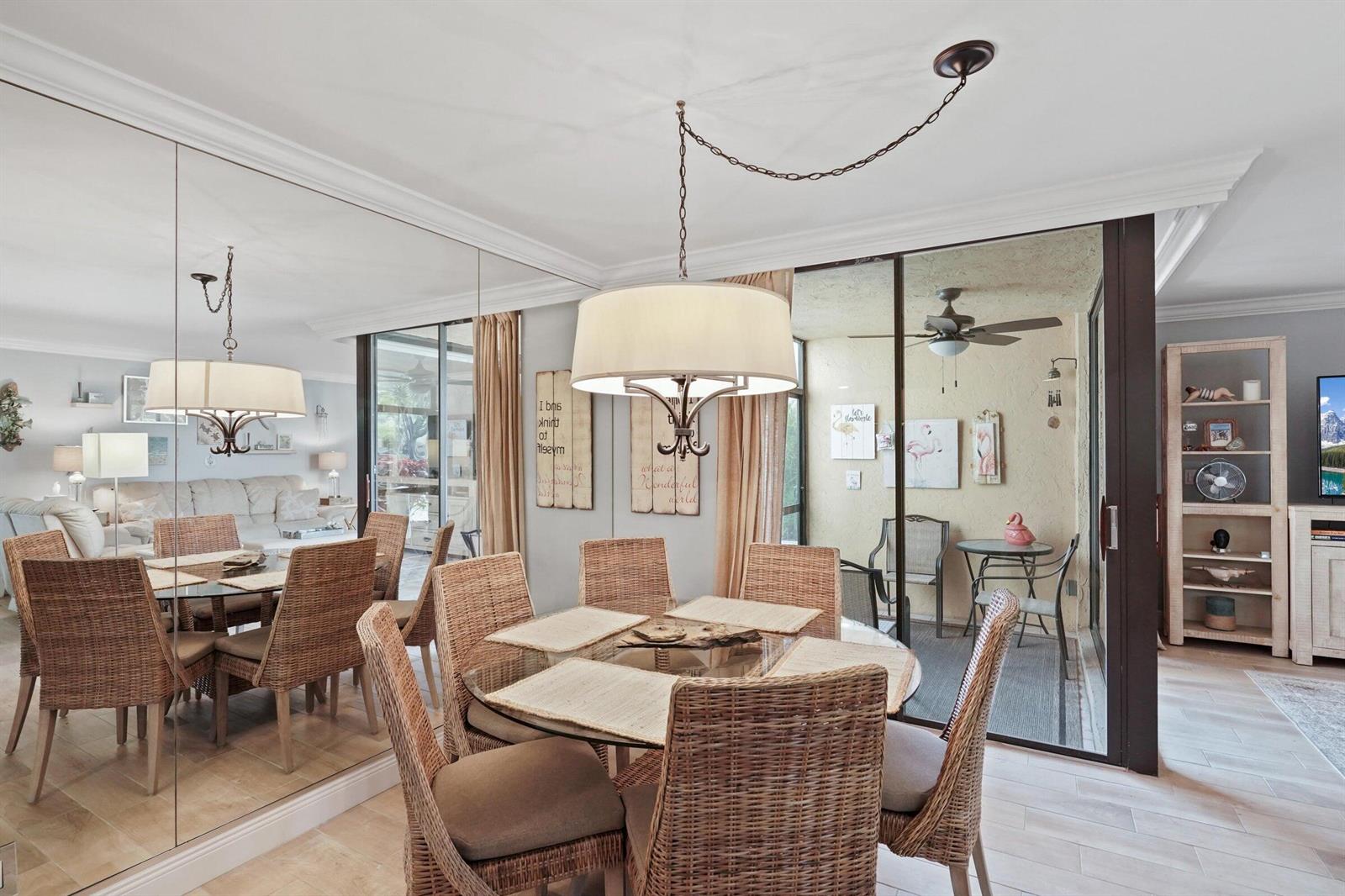 A dining room features a glass-topped wicker table, a drum chandelier, and a mirrored wall — 2255 Lindell Boulevard # 4105, Delray Beach FL 33444, DELRAY BEACH, FL