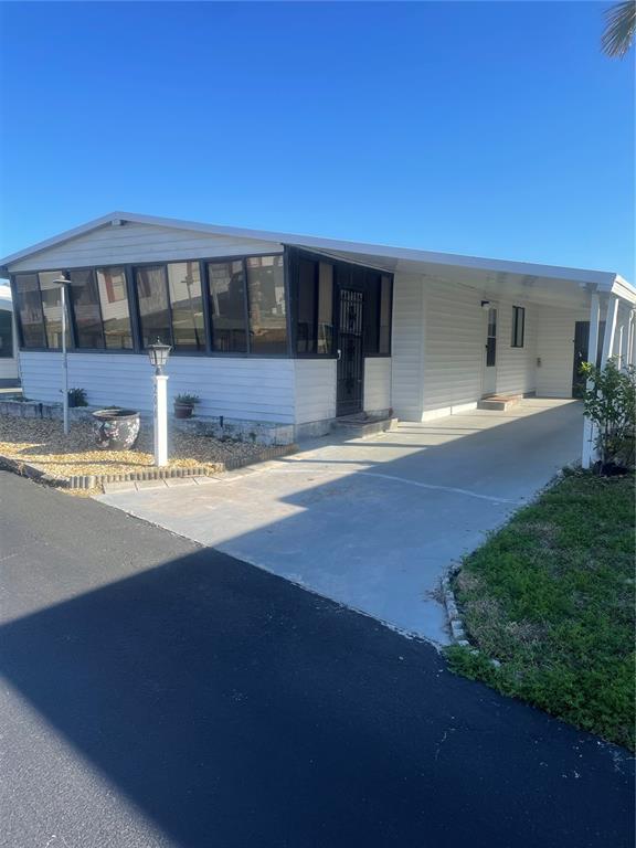 A white mobile home features a large enclosed porch, a concrete driveway, and a carport — 206 MONITOR DRIVE, FLAGLER BEACH, FL