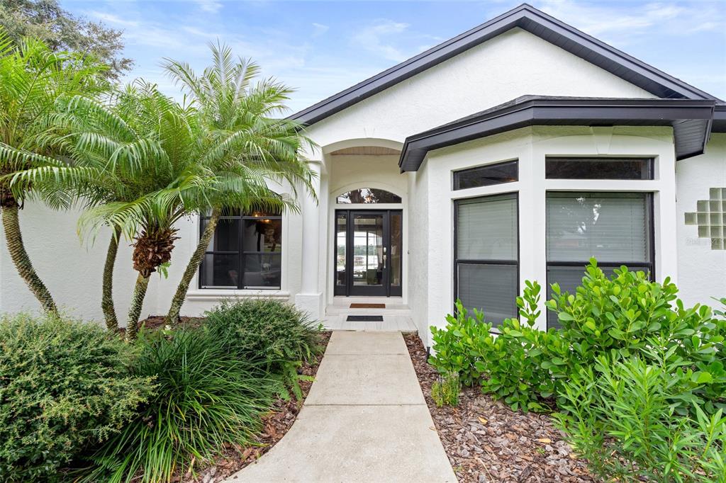 A white house exterior features a front walkway, a palm tree, and a glass-paneled door — 11210 CRESCENT BAY BOULEVARD, CLERMONT, FL