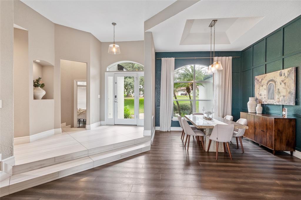 A dining room with dark wood floors, a green accent wall, and a raised entryway — 11210 CRESCENT BAY BOULEVARD, CLERMONT, FL
