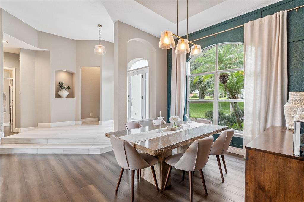 A dining room features a stone table, upholstered chairs, and a large window with curtains — 11210 CRESCENT BAY BOULEVARD, CLERMONT, FL