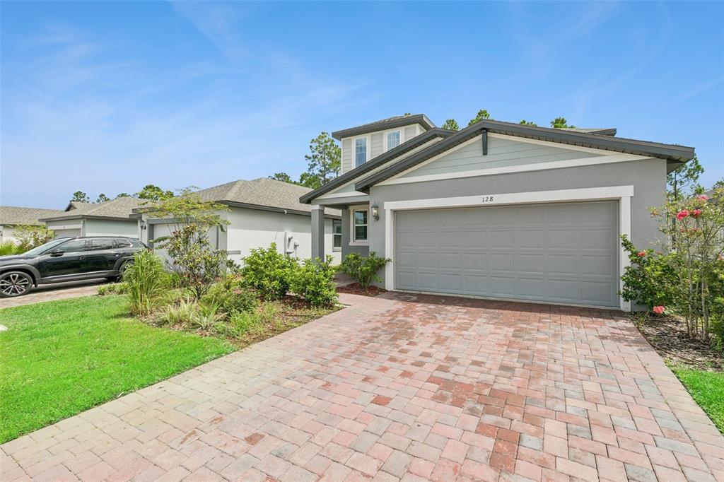 A single-story house with a gray exterior, a two-car garage, and a brick paver driveway — 128 LOST BALL DRIVE, DAYTONA BEACH, FL
