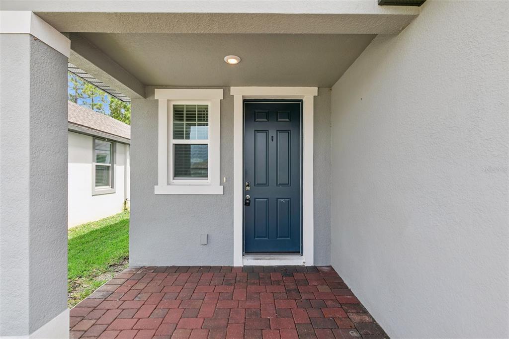 A covered entryway features a dark blue front door, a single window, and brick pavers — 128 LOST BALL DRIVE, DAYTONA BEACH, FL