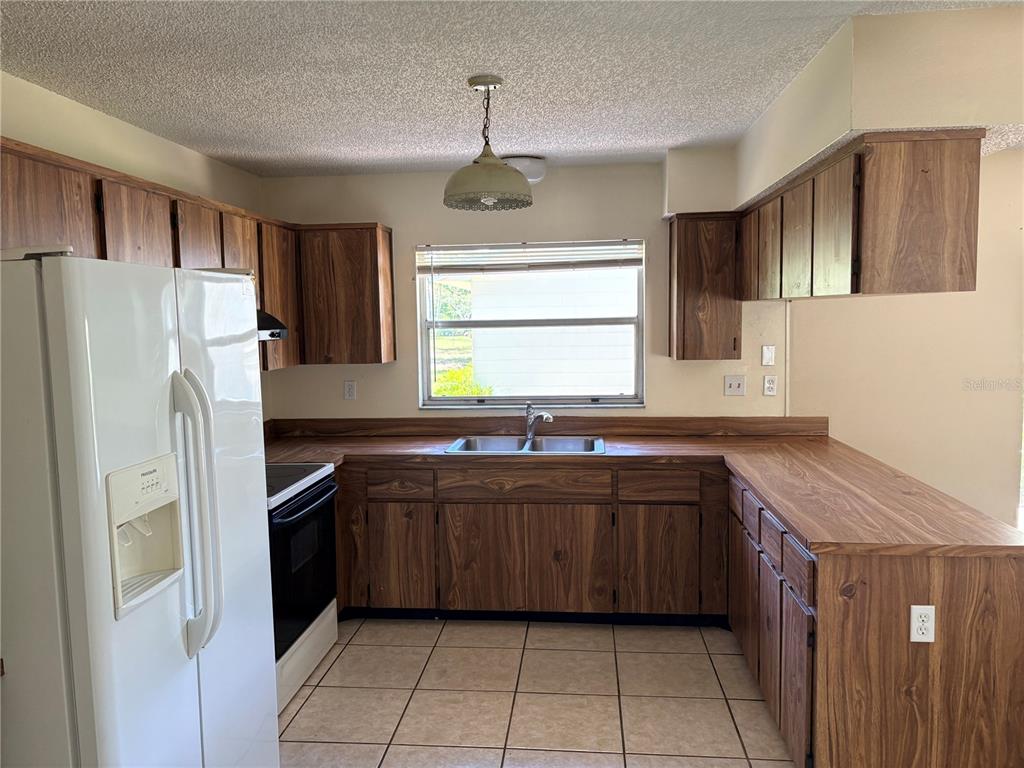 A kitchen features wood-grain cabinets, laminate countertops, a double-basin sink, and white appliances — 8907 WAYWARD CIRCLE, HUDSON, FL