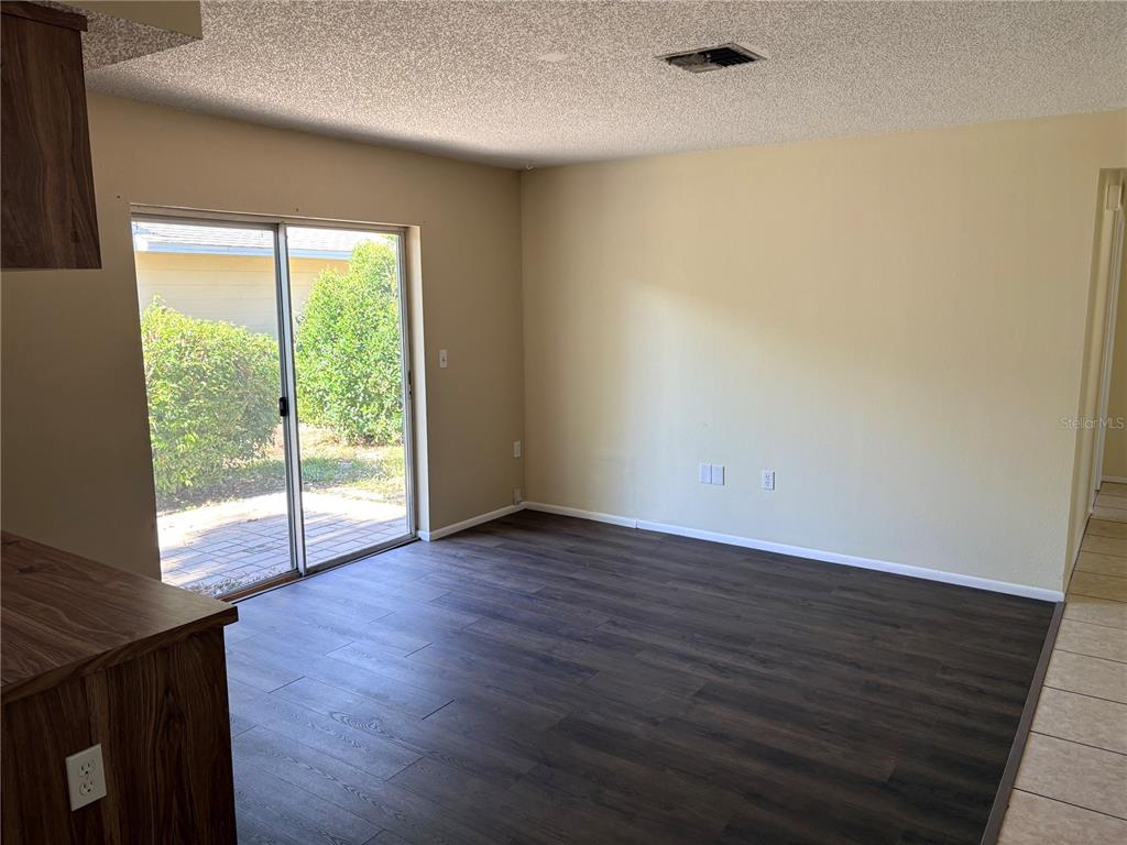 An empty room with dark wood-look flooring, beige walls, and a sliding glass door — 8907 WAYWARD CIRCLE, HUDSON, FL