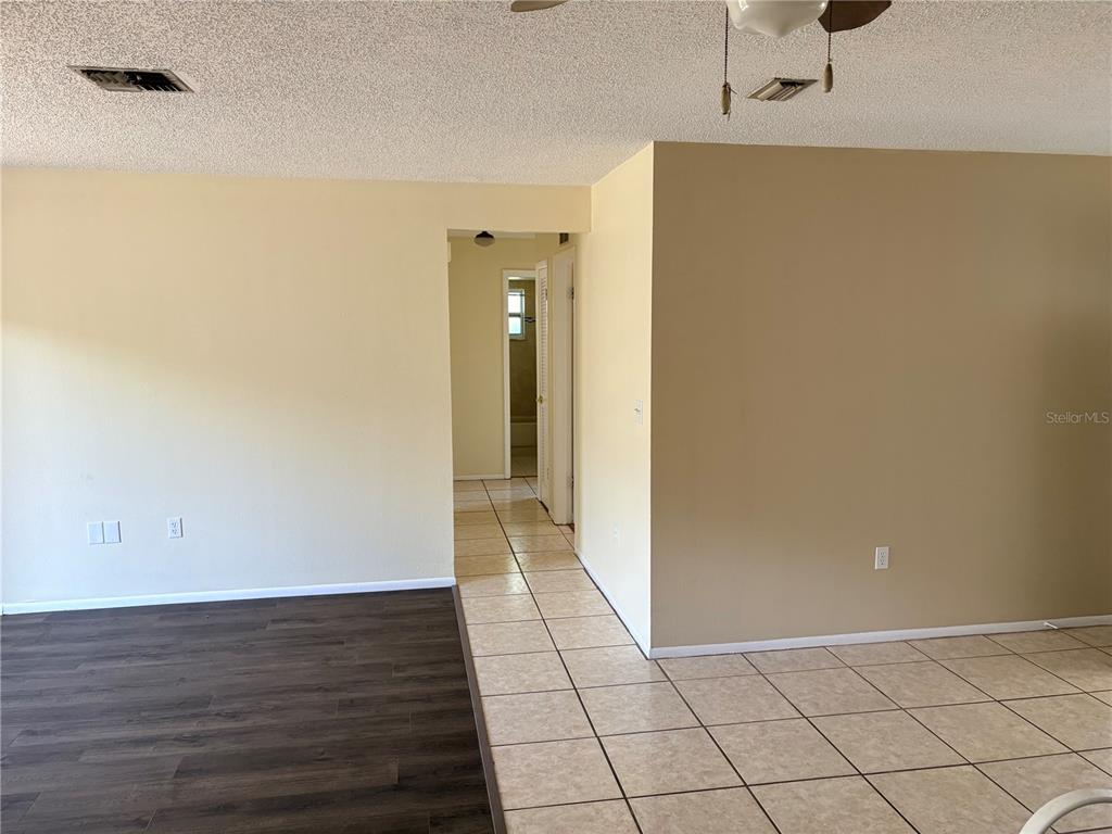 An interior view shows a room with wood-look flooring, tiled flooring, and a hallway entrance — 8907 WAYWARD CIRCLE, HUDSON, FL