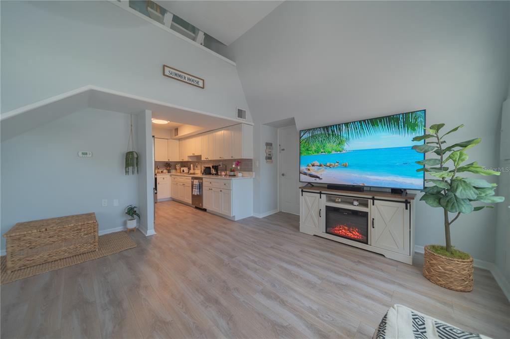 A living room with light wood floors, a fireplace media console, and an open kitchen — 501 PAMETO ROAD, NOKOMIS, FL
