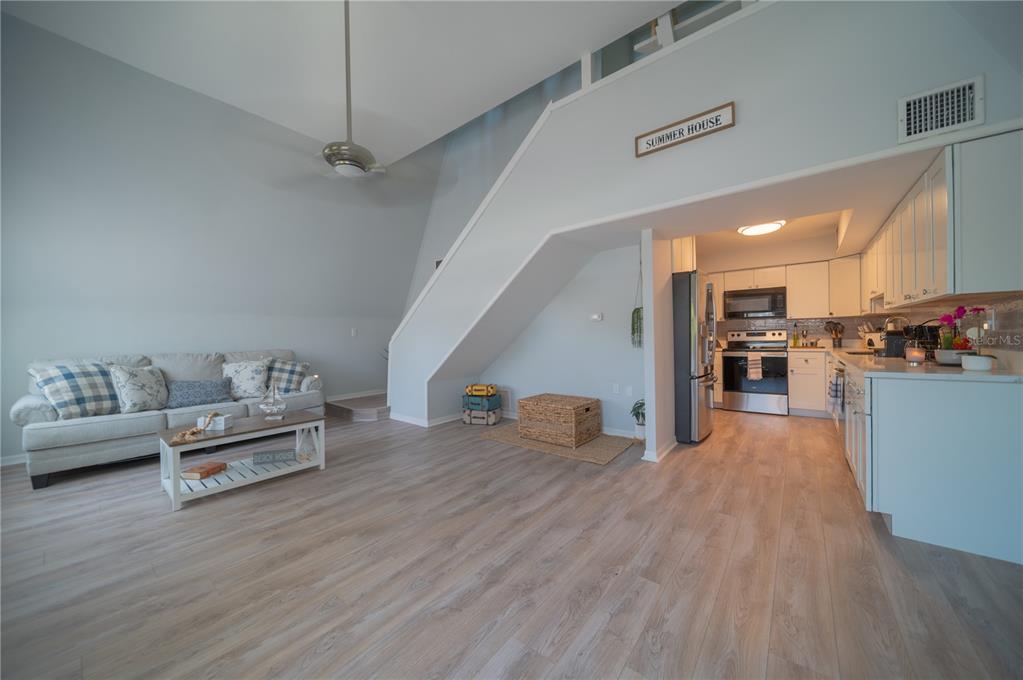 A living room with light wood flooring and a staircase leads to an open kitchen — 501 PAMETO ROAD, NOKOMIS, FL