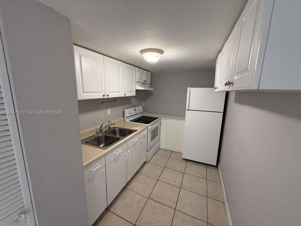A galley-style kitchen features white cabinets, a double sink, and white appliances — 6950 W 6th Ave # 509, Hialeah FL 33014, HIALEAH, FL