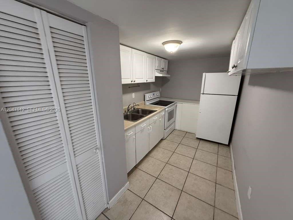 A galley kitchen features white cabinets, a white refrigerator, a stove, and tiled flooring — 6950 W 6th Ave # 509, Hialeah FL 33014, HIALEAH, FL