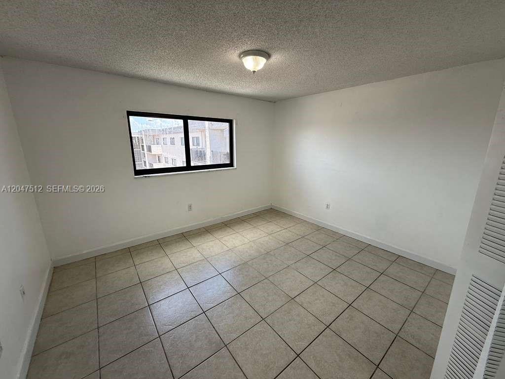 An empty bedroom features white walls, beige tile flooring, and a single window — 6950 W 6th Ave # 509, Hialeah FL 33014, HIALEAH, FL