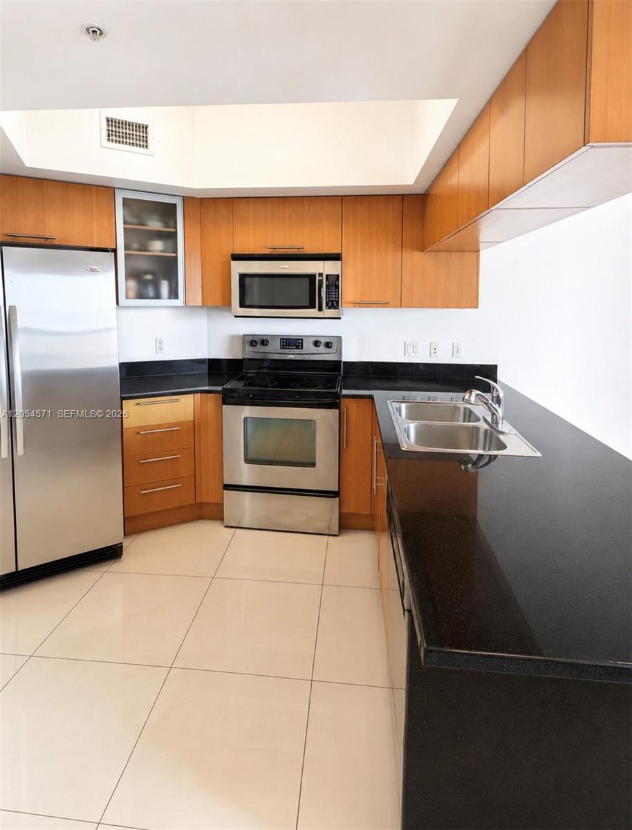 A kitchen features wood cabinets, stainless steel appliances, black countertops, and light tile flooring — 1750 N Bayshore Dr # 4201, Miami FL 33132, MIAMI, FL