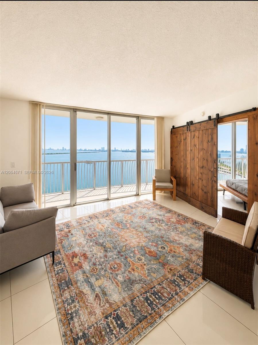 A living room with tile floors, a large area rug, and sliding doors overlooking water — 1750 N Bayshore Dr # 4201, Miami FL 33132, MIAMI, FL