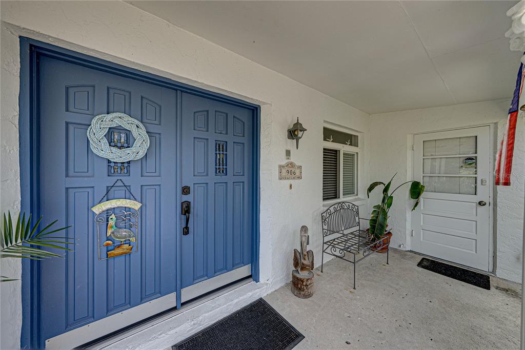 A covered porch features blue double front doors, a white side door, and a metal bench — 906 SAGO PALM WAY, APOLLO BEACH, FL