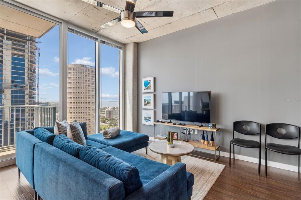 A modern living room features a blue sectional sofa, a television, and floor-to-ceiling windows — 777 N ASHLEY DRIVE UNIT 2308, TAMPA, FL