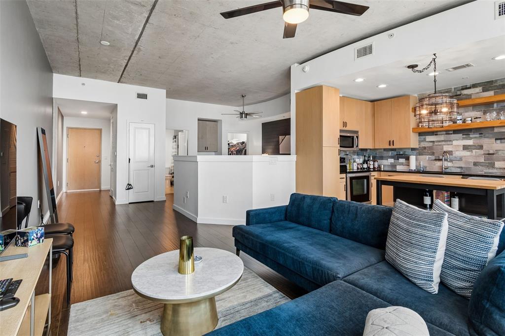 A modern open-concept living room and kitchen featuring a blue sectional sofa and concrete ceiling — 777 N ASHLEY DRIVE UNIT 2308, TAMPA, FL