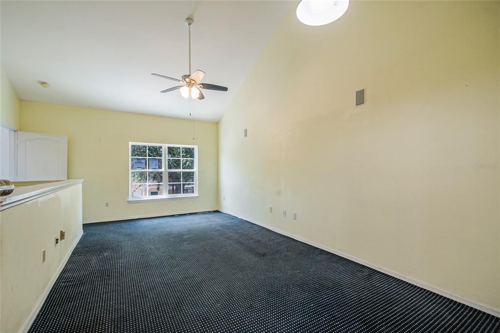 An empty room with vaulted ceilings, a ceiling fan, a large window, and dark carpeting — 3019 BONFIRE BEACH DRIVE UNIT 205, KISSIMMEE, FL