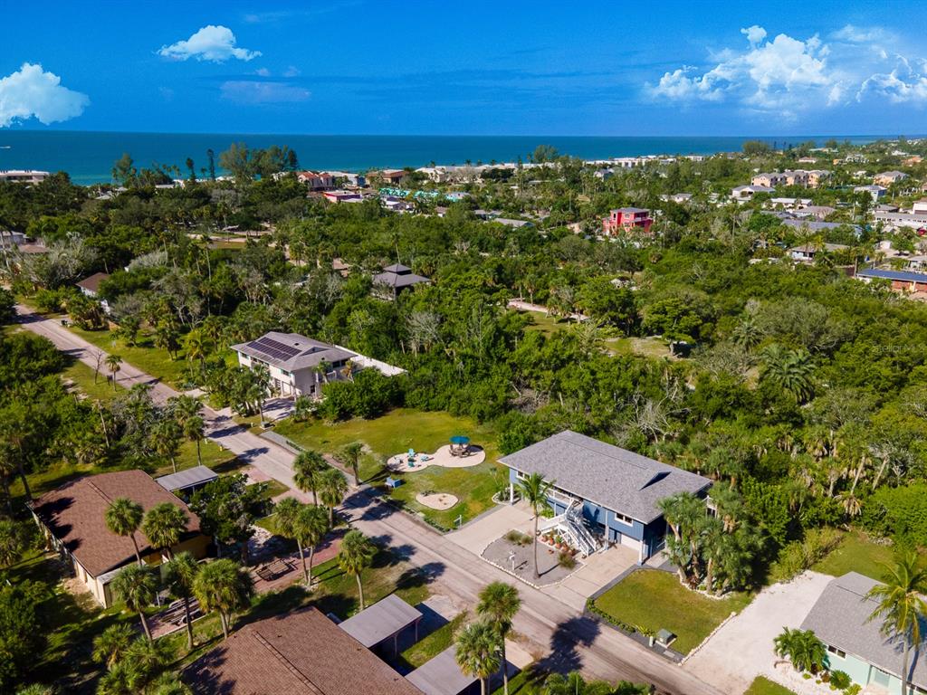 An aerial view shows several houses surrounded by dense trees near a coastal beach — 681 GULF BAY ROAD, LONGBOAT KEY, FL