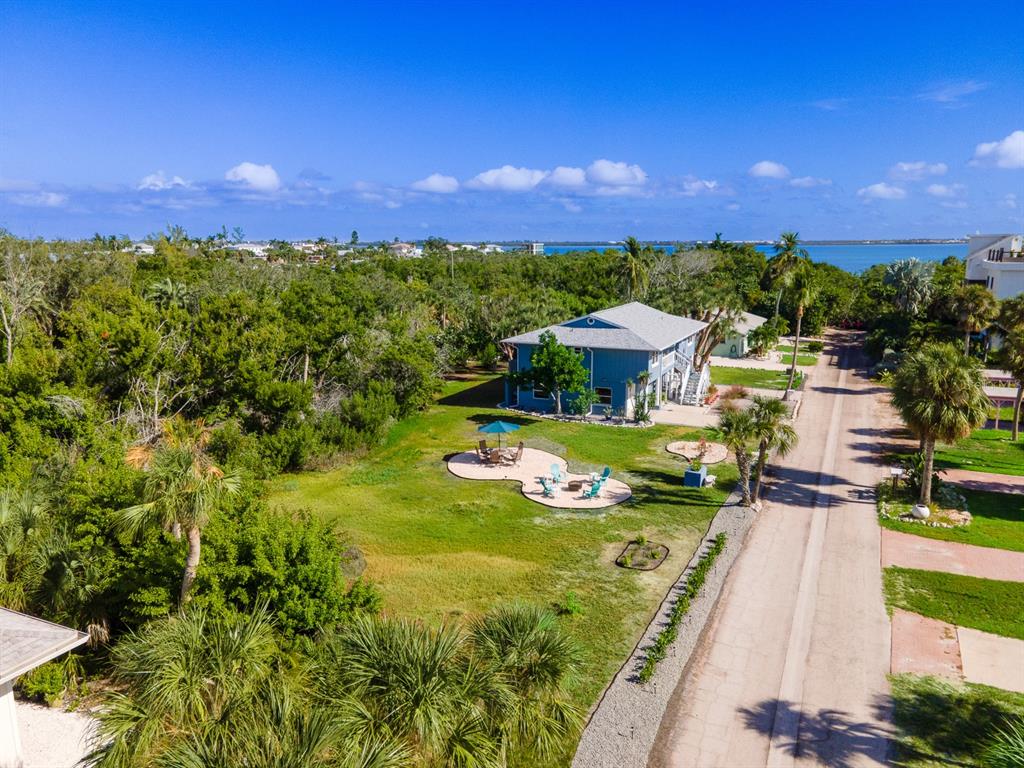 An aerial view shows a blue house with a patio area near a coastal road — 681 GULF BAY ROAD, LONGBOAT KEY, FL