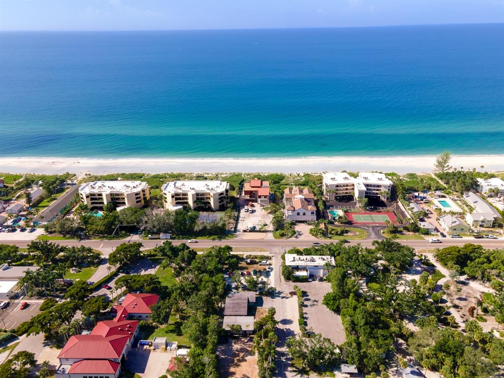 An aerial view shows beachfront condominiums and houses along a coastline with turquoise water — 681 GULF BAY ROAD, LONGBOAT KEY, FL