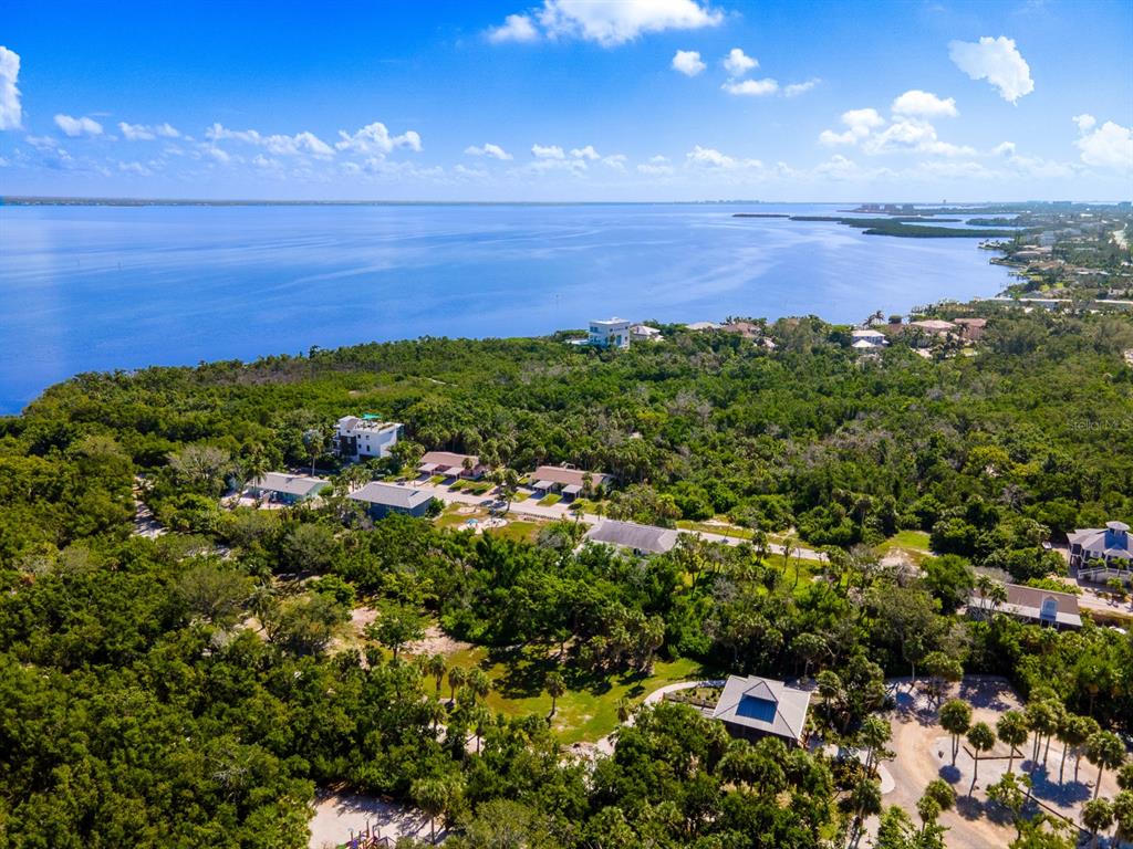 An aerial view shows several houses nestled within a dense forest bordering a large bay — 681 GULF BAY ROAD, LONGBOAT KEY, FL