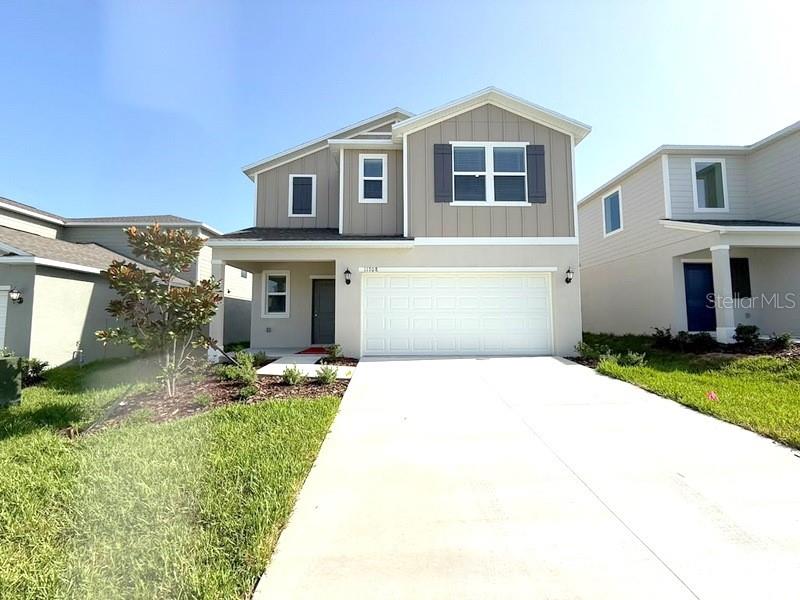 A two-story house with a beige exterior, a white garage door, and a concrete driveway — 11708 NOBLE BLOSSOM LOOP, DADE CITY, FL