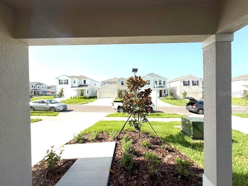 A view from a covered porch looking out at a suburban street with houses — 11708 NOBLE BLOSSOM LOOP, DADE CITY, FL