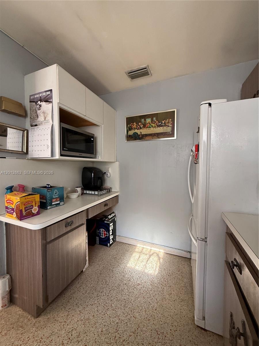A kitchen features white cabinets, a microwave, a refrigerator, and a framed wall art piece — 399 W 12th St, Hialeah FL 33010, HIALEAH, FL