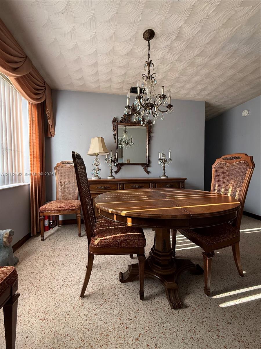 A dining room features a round wooden table, cane-back chairs, a chandelier, and a sideboard — 399 W 12th St, Hialeah FL 33010, HIALEAH, FL
