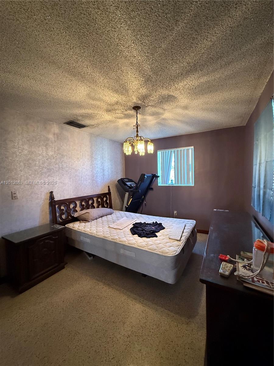 A bedroom features a bed, a treadmill, a chandelier, and textured walls and ceilings — 399 W 12th St, Hialeah FL 33010, HIALEAH, FL