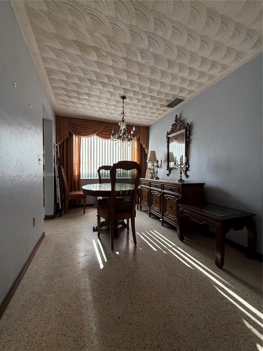 A dining room features a textured ceiling, a chandelier, a wooden sideboard, and terrazzo flooring — 399 W 12th St, Hialeah FL 33010, HIALEAH, FL