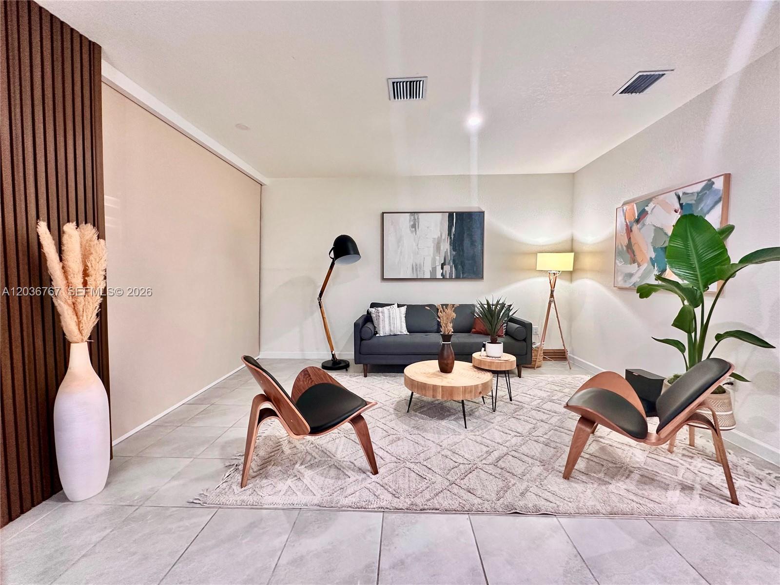A modern living room features a dark sofa, two wooden chairs, and a textured rug — HIALEAH, FL