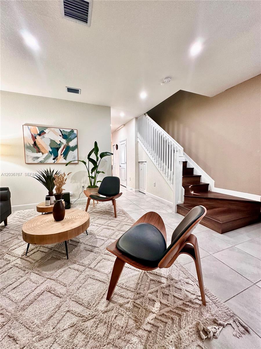 A living room features a wooden staircase, two mid-century modern chairs, and a round table — HIALEAH, FL