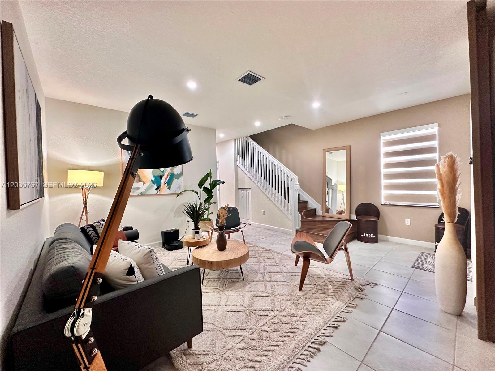 A living room features a dark sofa, two wooden chairs, a staircase, and tiled floors — HIALEAH, FL