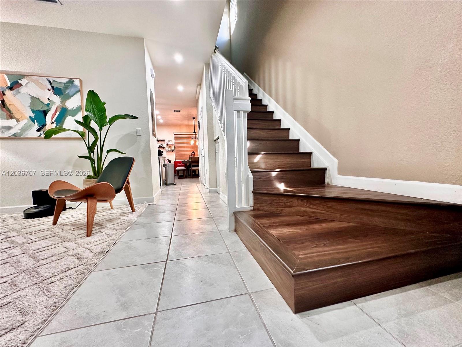 A hallway features light tile flooring, a wooden staircase, and a modern accent chair — HIALEAH, FL