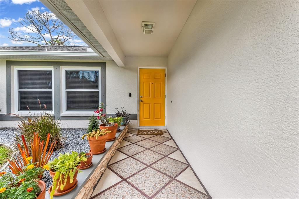 A front entryway features a yellow door, a tiled porch, and several potted plants — 3178 ALBENGA LANE, NORTH PORT, FL