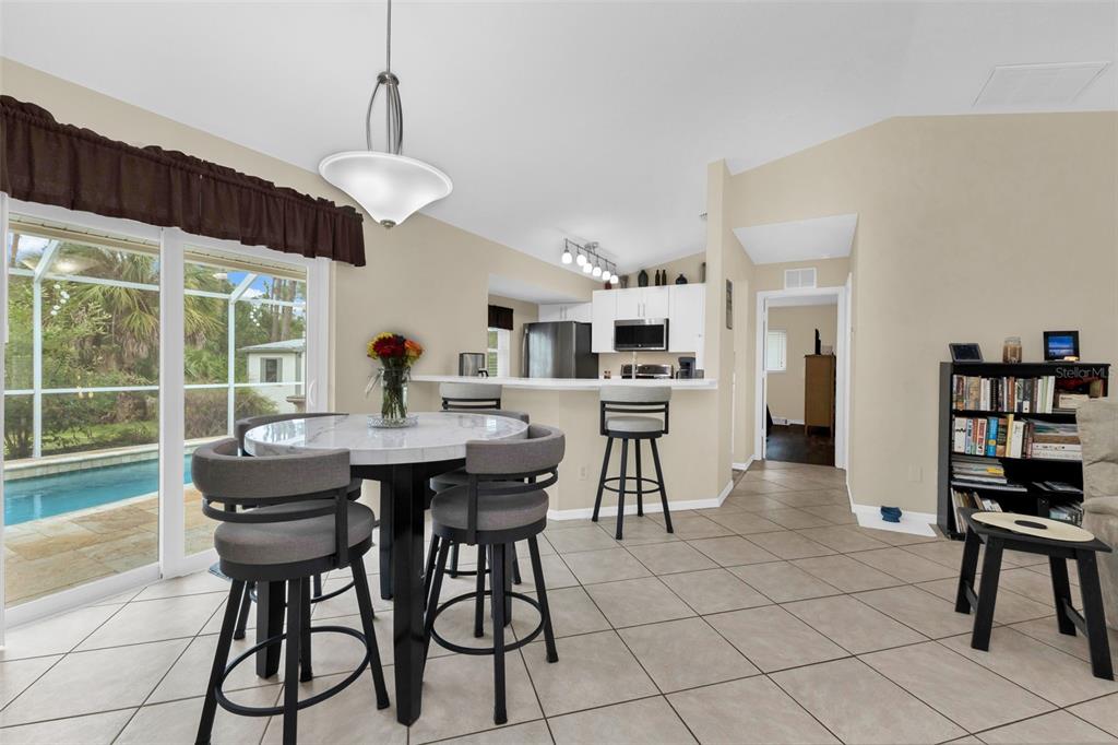 A dining area with a round table, bar stools, and a view of a swimming pool — 3178 ALBENGA LANE, NORTH PORT, FL