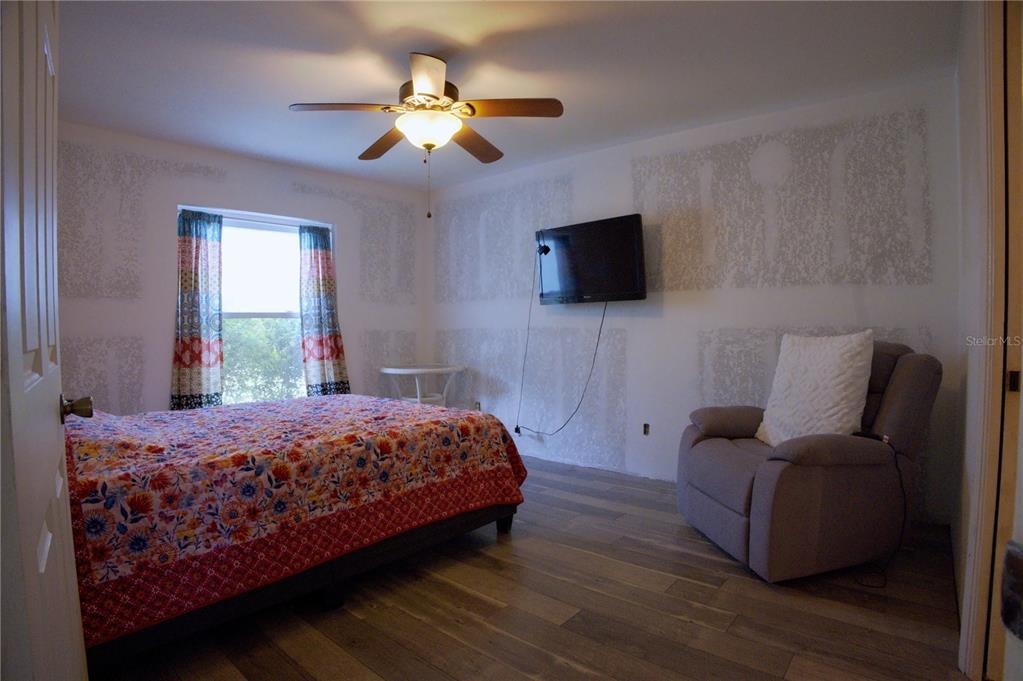 A bedroom features a bed with a floral quilt, a recliner, and a wall-mounted television — 4621 ELDRON, NORTH PORT, FL