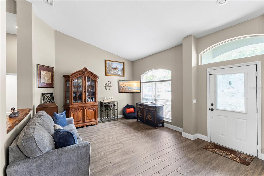 A living room features wood-look tile flooring, a gray sofa, and a large wooden hutch — 4038 LITHIA RIDGE BOULEVARD, VALRICO, FL