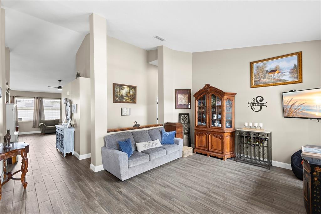 A living room features gray wood-look tile flooring, a gray sofa, and a wooden hutch — 4038 LITHIA RIDGE BOULEVARD, VALRICO, FL