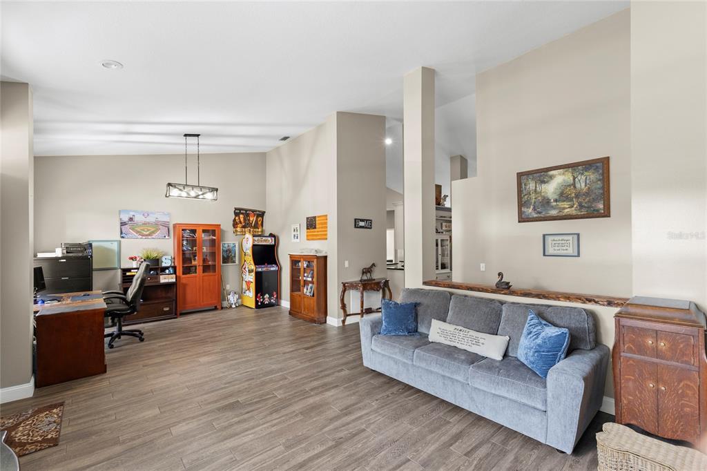 A living room and office space feature wood-look flooring, a grey sofa, and an arcade cabinet — 4038 LITHIA RIDGE BOULEVARD, VALRICO, FL