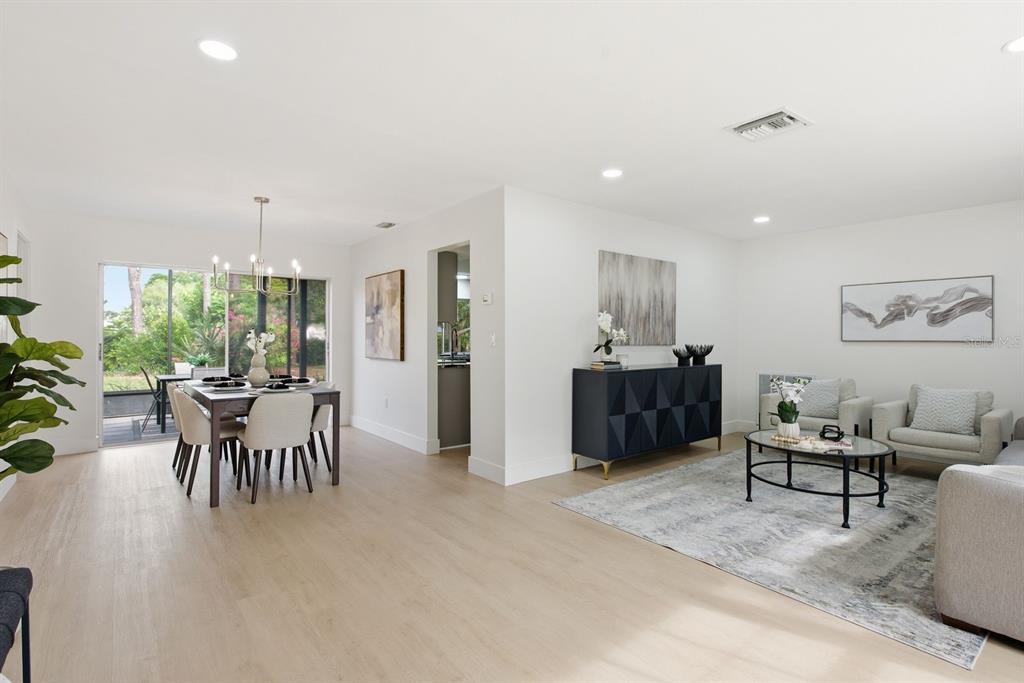 An open-concept living and dining area features light wood floors, white walls, and sliding doors — 13013 SPICEBOX WAY, HUDSON, FL