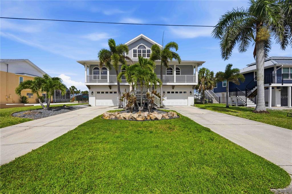 A two-story coastal home with a raised main level, dual garages, and palm trees — 10460 MARION STREET, ENGLEWOOD, FL