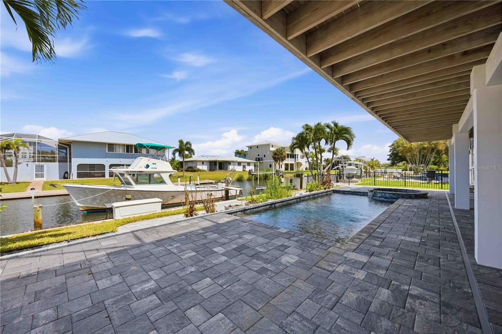 A paved patio features a small swimming pool overlooking a canal with a docked boat — 10460 MARION STREET, ENGLEWOOD, FL