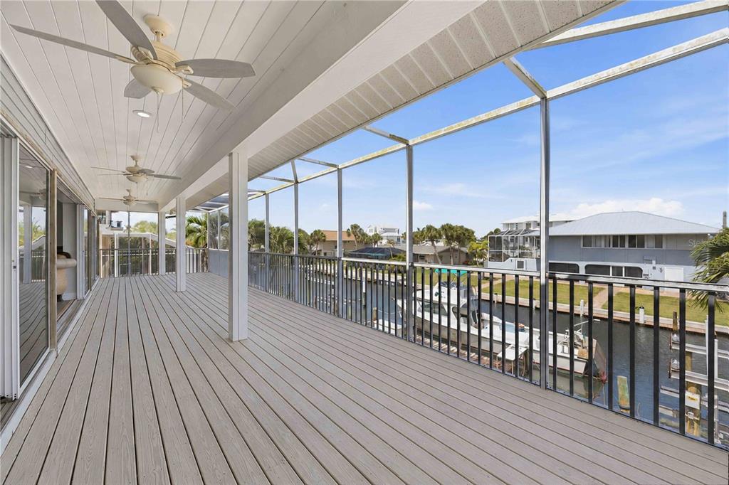 A screened-in balcony with light wood decking overlooks a canal with a docked boat — 10460 MARION STREET, ENGLEWOOD, FL