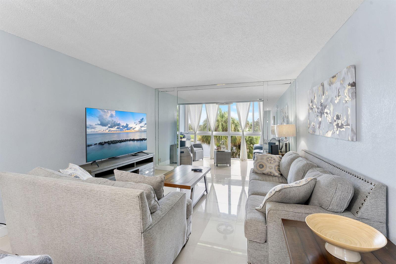 A living room features light gray sofas, a television, and a balcony with palm trees — 7807 Golf Cir Drive # 305, Margate FL 33063, MARGATE, FL
