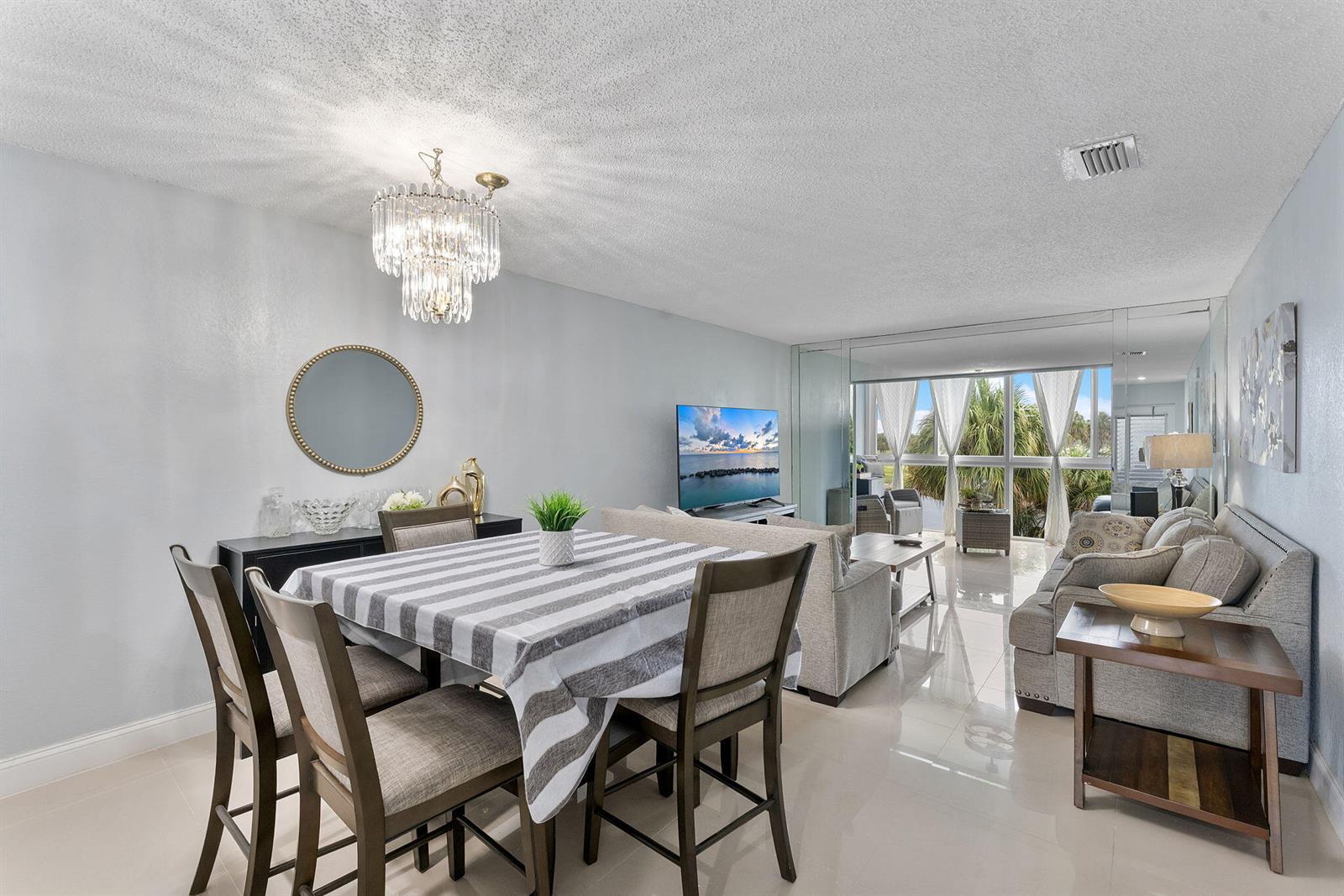 A dining area and living room with tile floors, a crystal chandelier, and large windows — 7807 Golf Cir Drive # 305, Margate FL 33063, MARGATE, FL