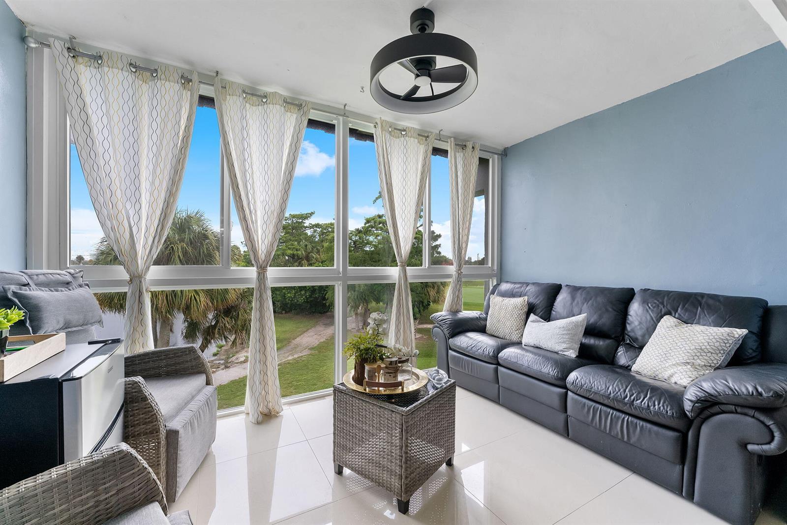 A sunroom features a black leather sofa, wicker furniture, tile flooring, and floor-to-ceiling windows — 7807 Golf Cir Drive # 305, Margate FL 33063, MARGATE, FL